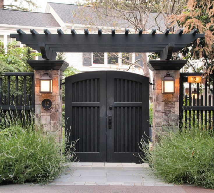 an entrance to a home with stone pillars and black gates, surrounded by greenery