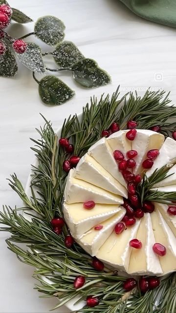 a piece of cheese with pomegranates is on a platter surrounded by greenery