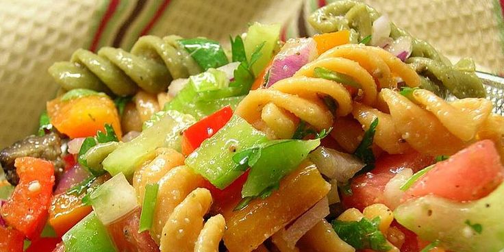 a bowl filled with pasta and vegetables on top of a cloth covered table next to a fork