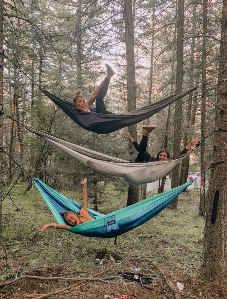 two women are laying in hammocks in the woods, one is upside down