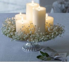 three white candles sitting on top of a cake plate with baby's breath flowers