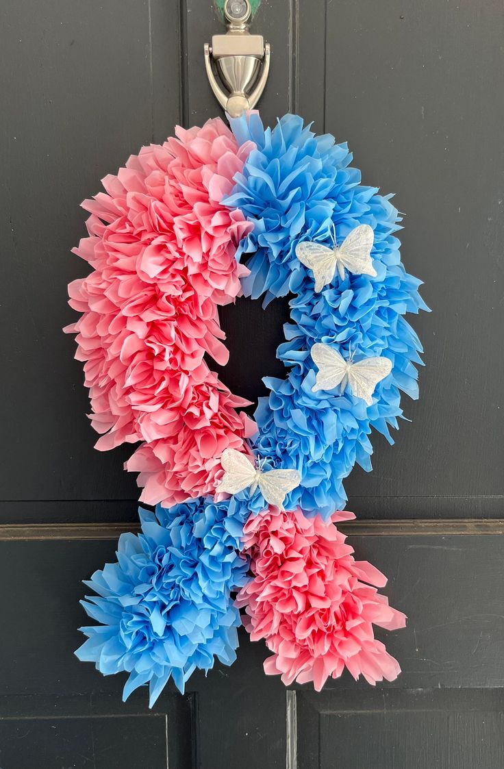 a wreath with pink, blue and white flowers hanging on the front door to welcome guests