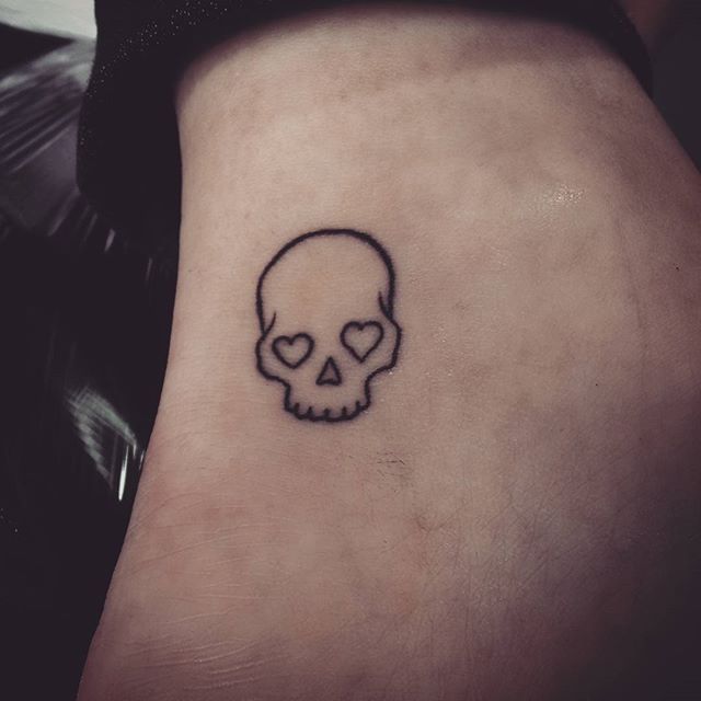 a small skull tattoo on the back of a woman's left leg, with a heart in it