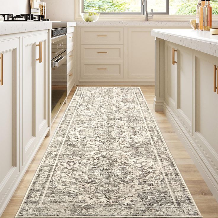 a kitchen with white cabinets and an area rug on the floor in front of a window