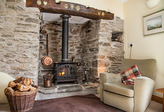 a living room with stone walls and a wood burning stove in the corner next to a chair