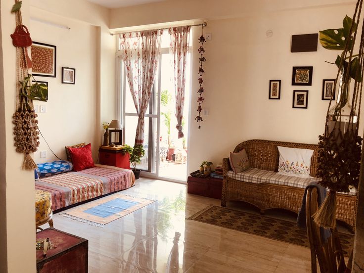 a living room filled with furniture next to a window covered in plants and pictures on the wall