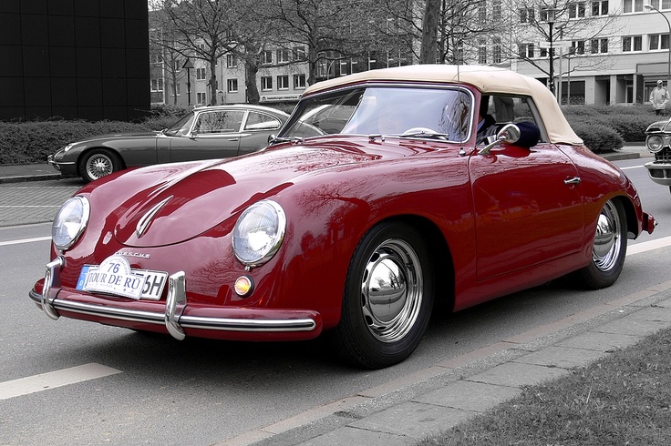 an old red sports car parked on the side of the road in front of some buildings