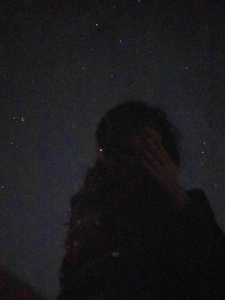 a woman covering her face in front of the night sky with stars behind her head