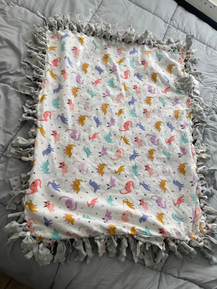 a blanket that is laying on top of a bed with white sheets and multicolored animals