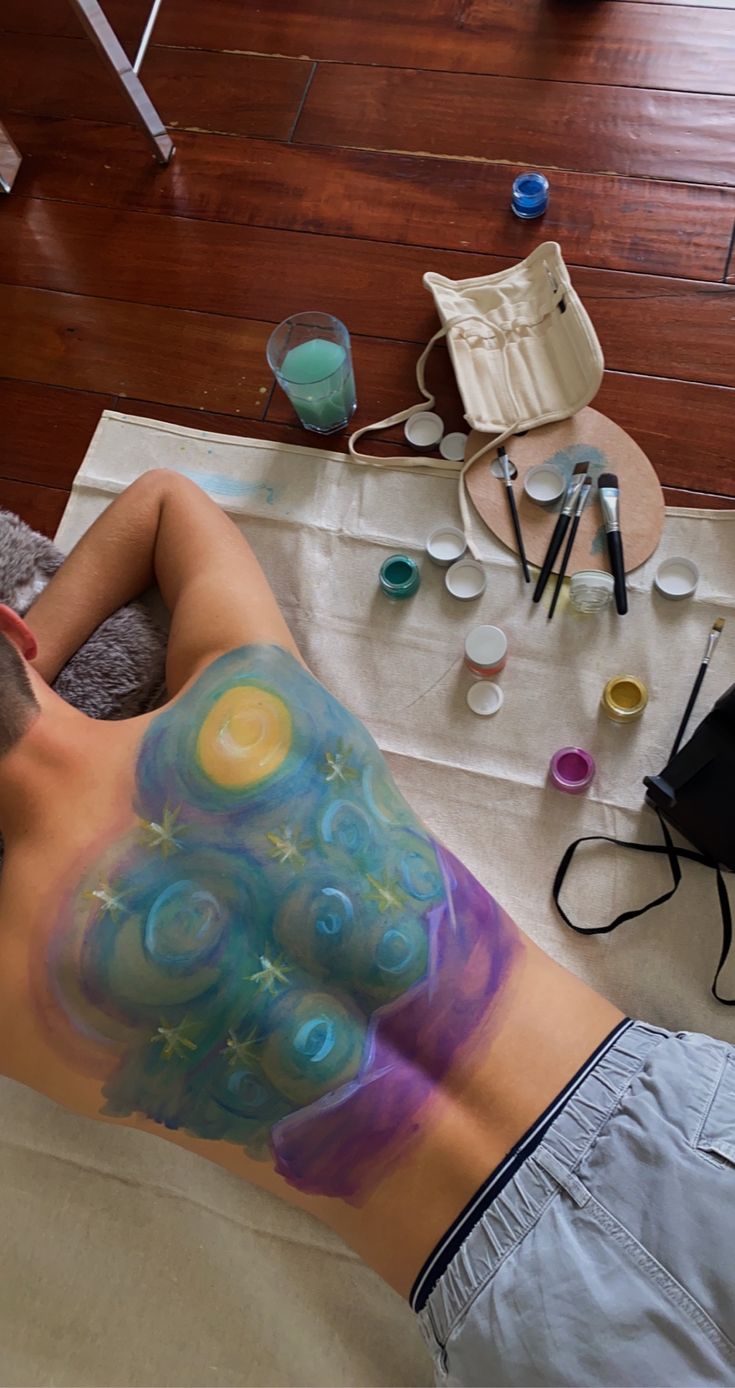 a man laying on top of a bed covered in lots of paint next to other items