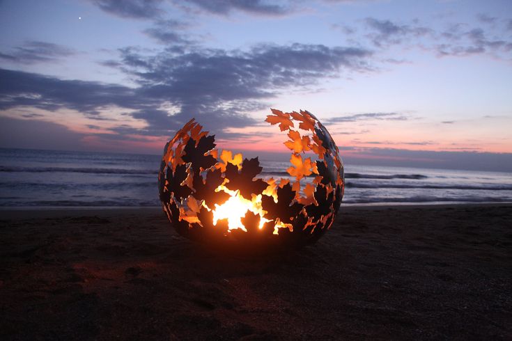 a fire pit on the beach with leaves around it at sunset or dawn, in front of an ocean