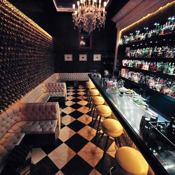 a bar with black and white checkered flooring, chandelier and shelves full of liquor bottles