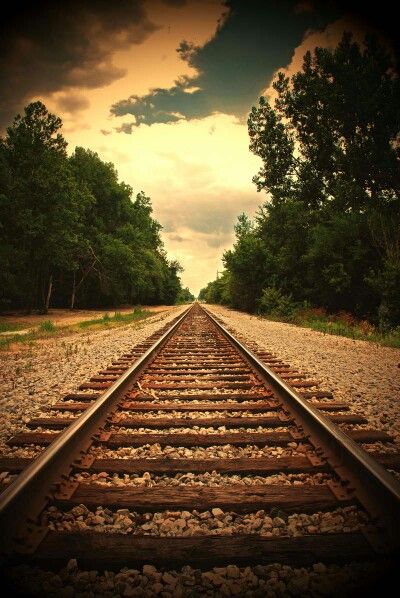 an old railroad track stretching into the distance with trees on either side and clouds in the background