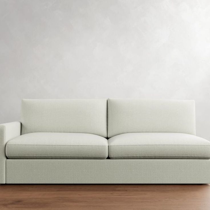 a white couch sitting on top of a wooden floor in front of a gray wall