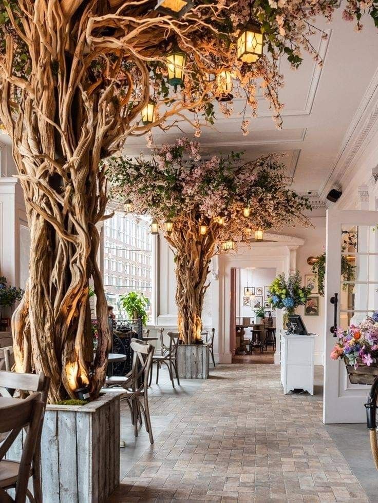 the inside of a restaurant with tables, chairs and trees in blooming branches hanging from the ceiling