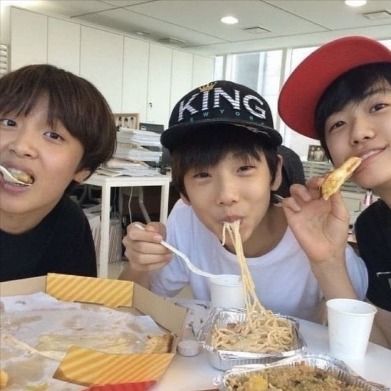 three people sitting at a table with food in front of them and one person eating noodles