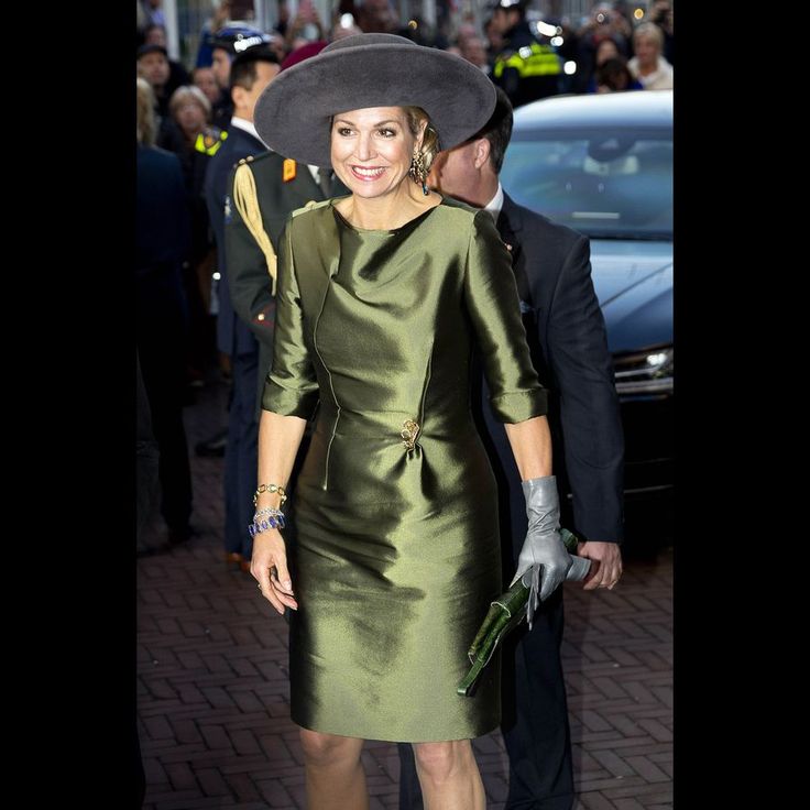 a woman in a green dress and hat walking down the street with other people behind her