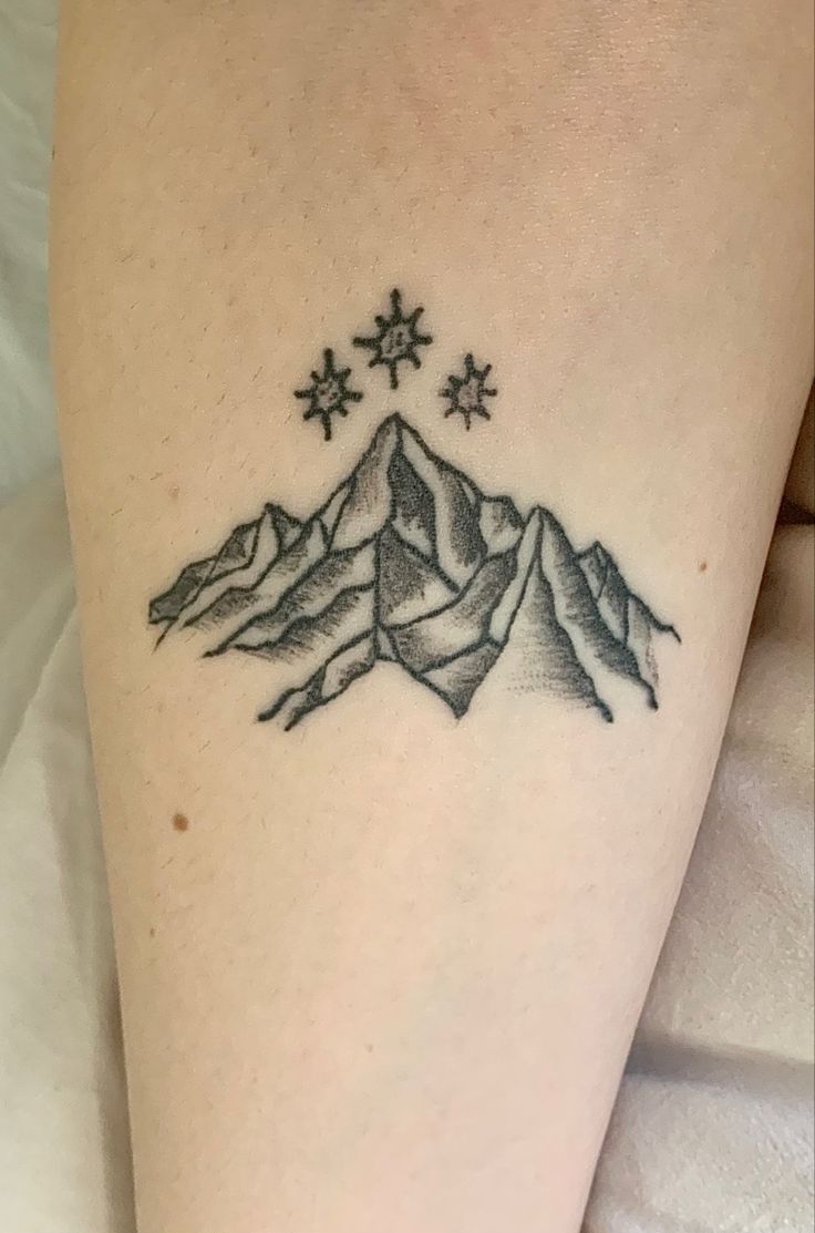 a tattoo on the leg of a woman with mountains and stars in the sky above it