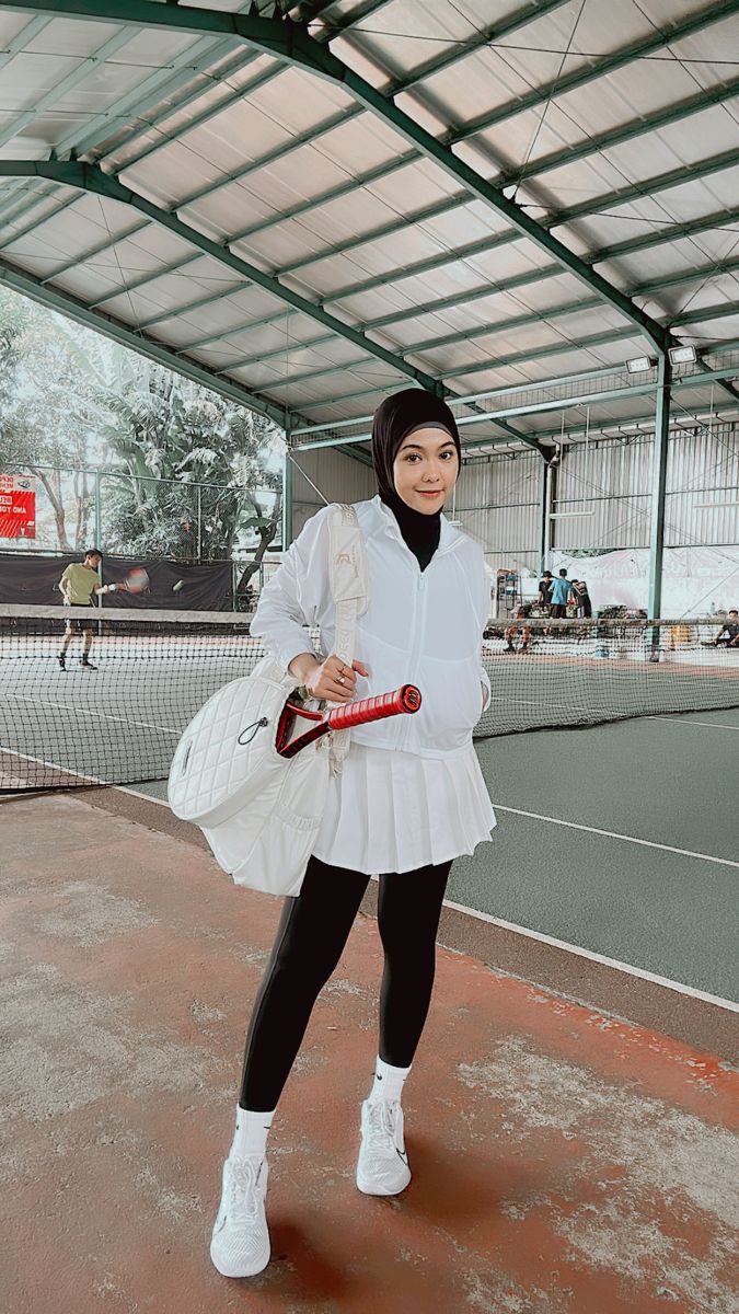 a woman standing on a tennis court holding a racquet in one hand and a bag in the other