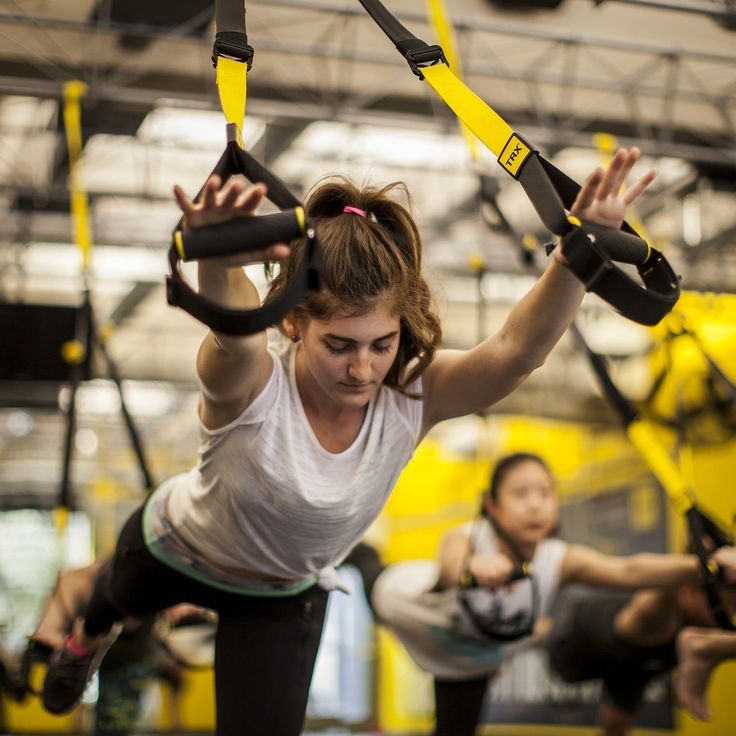 a group of people doing aerial exercises in a gym with yellow straps on their hands