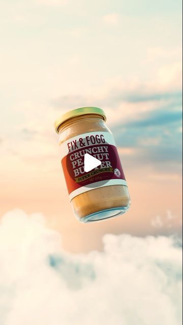 a jar of peanut butter flying through the air with clouds in the backgroud