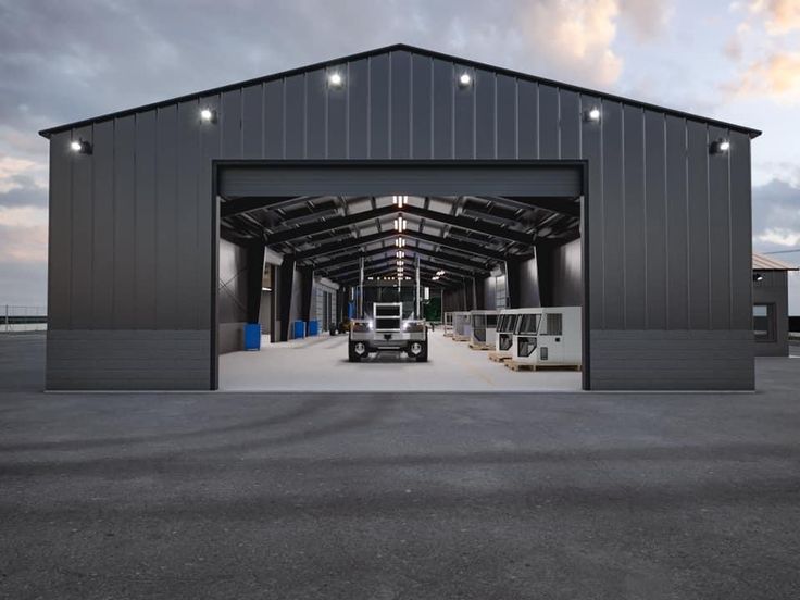 a truck is parked in front of a large garage with its doors open and lights on