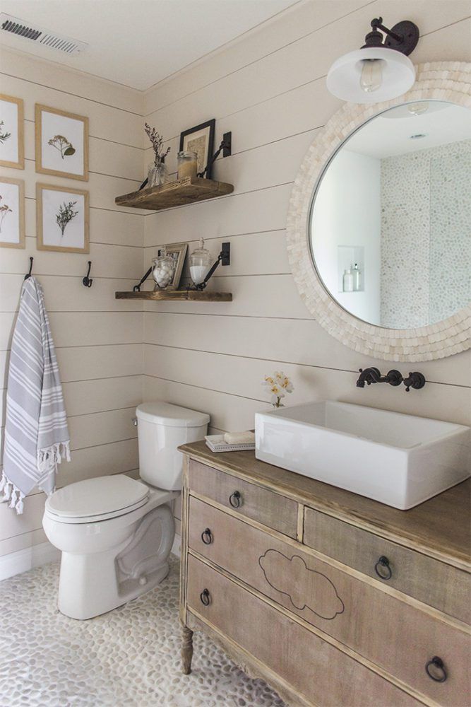 a white toilet sitting next to a wooden dresser in a bathroom under a round mirror