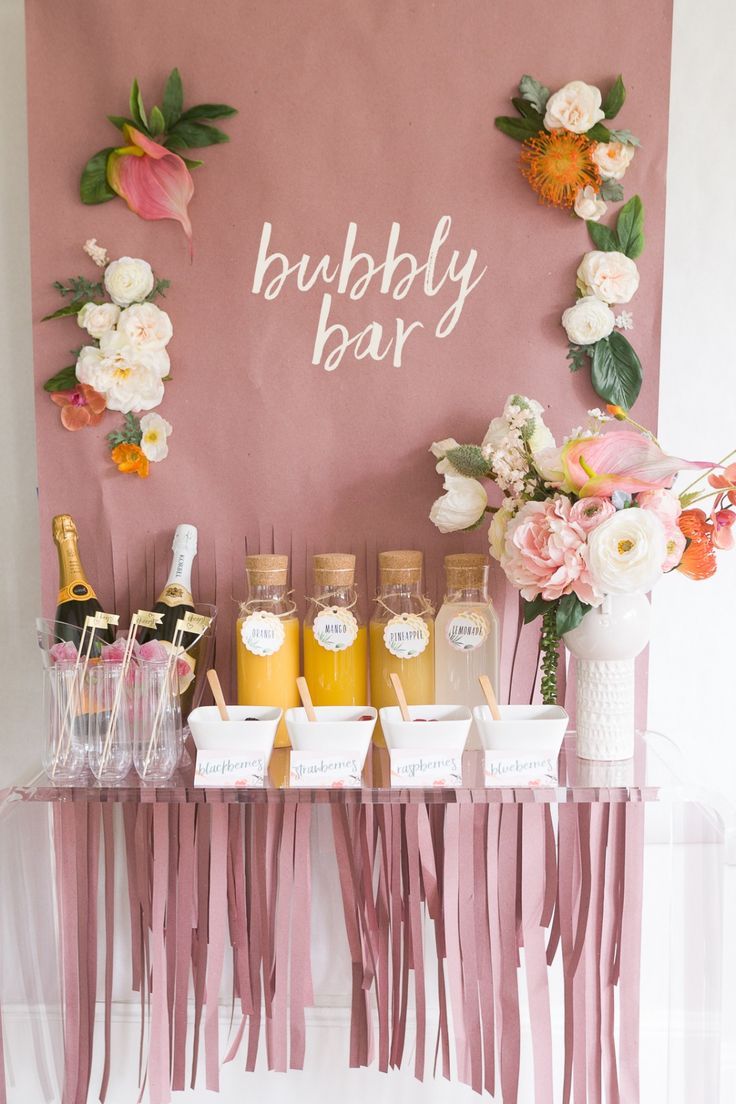 a table topped with lots of drinks next to a pink sign that says bubbly bar