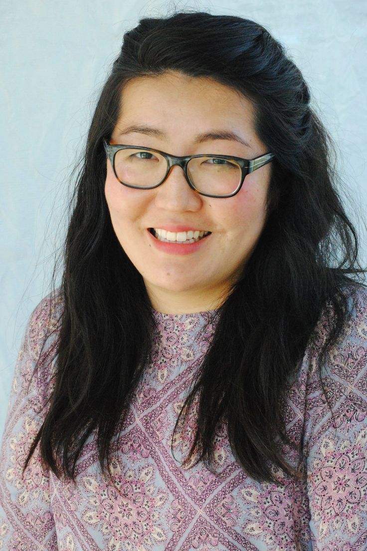 a woman with glasses smiling for the camera while wearing a purple shirt and black rimmed glasses