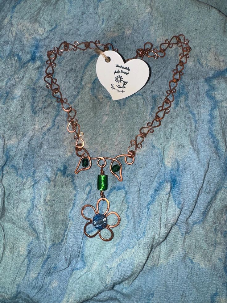 This beautifully unique and one of kind necklace features a handcrafted copper flower with a blue silver lined lampwork glass bead at the center and green lampwork glass beads in the stylized stem and leaves of the flower. The links in the chain and the hook clasp are hand formed and hammered individually, and assembled from 99.9% pure copper, assuring that it is 100% free of zinc and nickel. This would make the perfect gift for any occasion, however copper is an icon of strength, beauty, and wealth for your seventh anniversary! Silver Line, Wedding Jewellery Necklace, Hook Clasp, Lampwork Glass Beads, Pure Copper, Flower Necklace, Wedding Necklace, Glass Bead, Blue And Silver