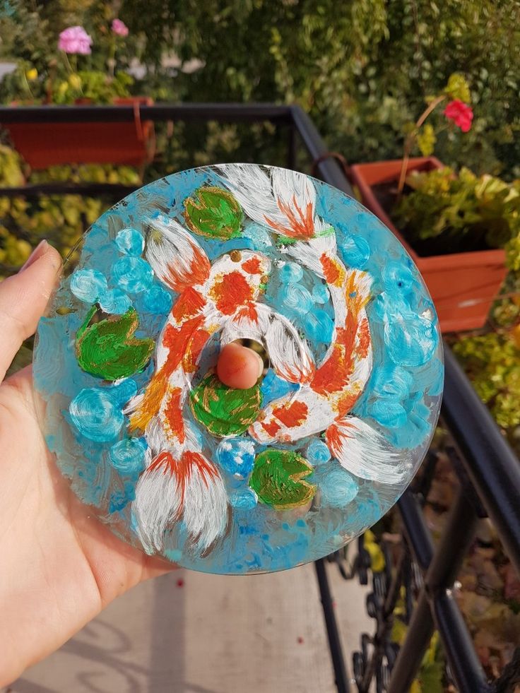 a hand holding up a glass plate with fish on it in front of some plants