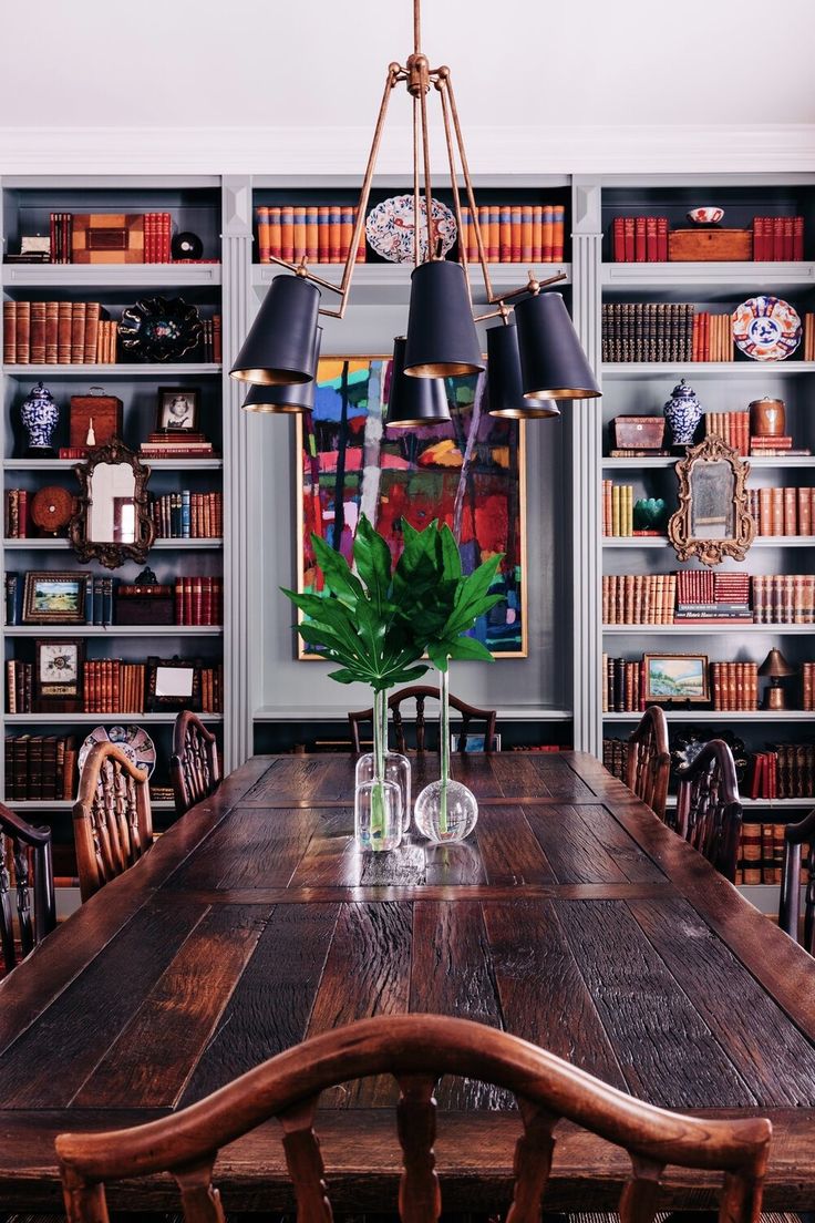 a dining room table surrounded by bookshelves and vases with plants in them