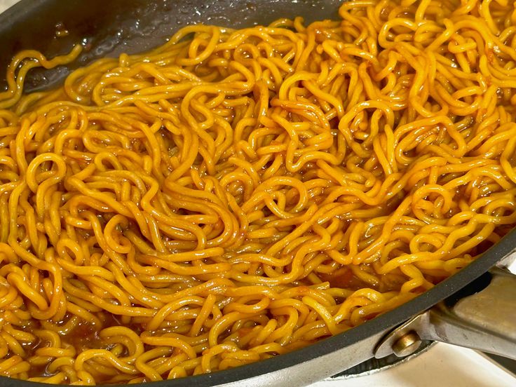 noodles are being cooked in a wok on the stove