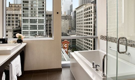 a bathroom with a tub, sink and large window overlooking the skyscrapers in new york city