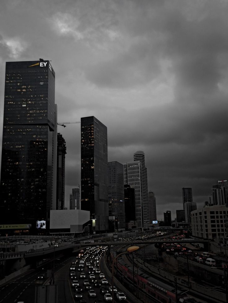 the city skyline is dark and cloudy as cars drive down the road in front of it