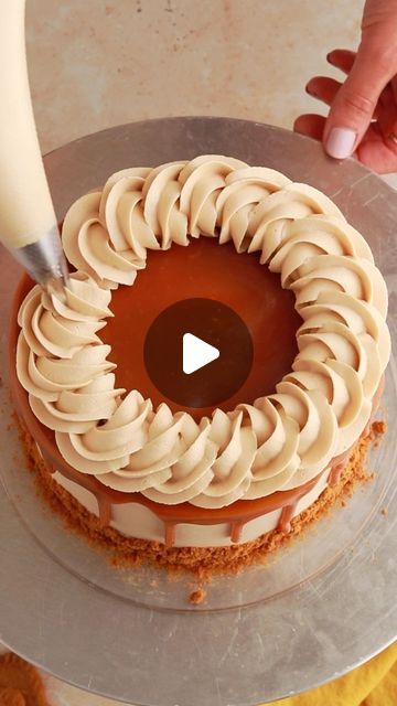 someone is decorating a cake with white icing and caramel swirls on it