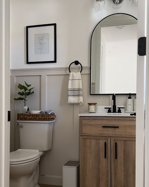 a white toilet sitting next to a bathroom sink under a mirror and a wooden cabinet