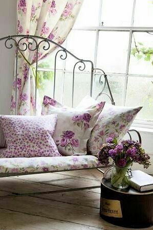 a couch with pillows and flowers on it in front of a window