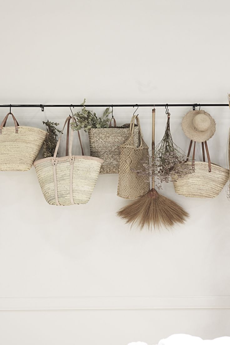 several straw bags hanging on a wall with plants in the bottom right hand corner and two hats hanging from hooks