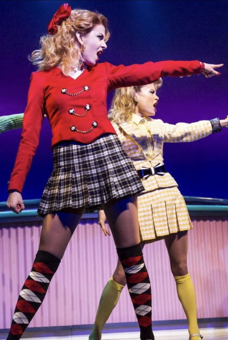 two women in plaid skirts and red sweaters are performing on stage with their arms stretched out