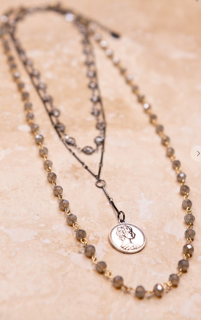 a necklace with a coin on it sitting on top of a marble table next to a chain