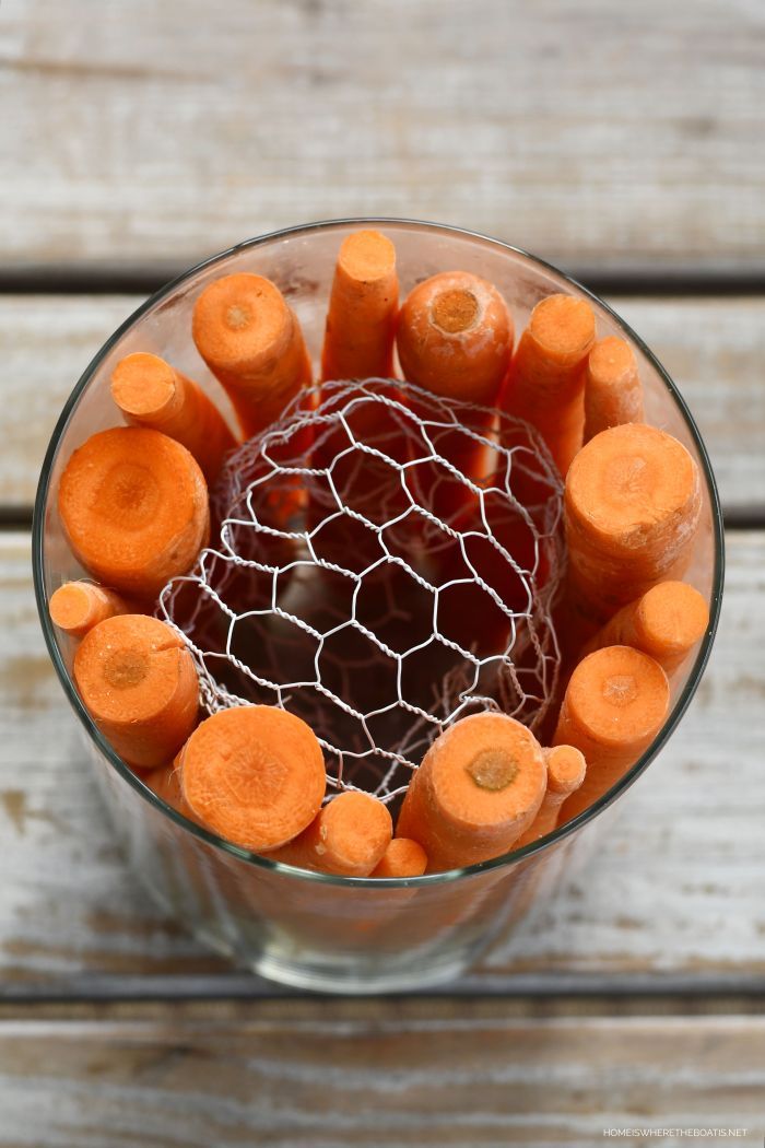 carrots in a glass bowl with a net on top sitting on a wooden table