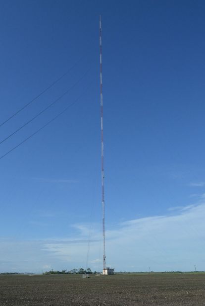 a large antenna on top of a pole in the middle of an open field with power lines