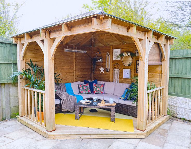 a wooden gazebo with couches and tables in the middle of an outdoor area