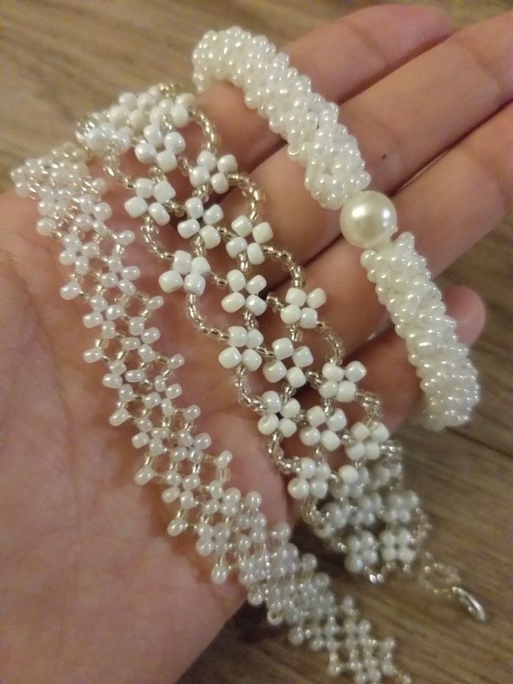 the hand is holding three bracelets with pearls on them