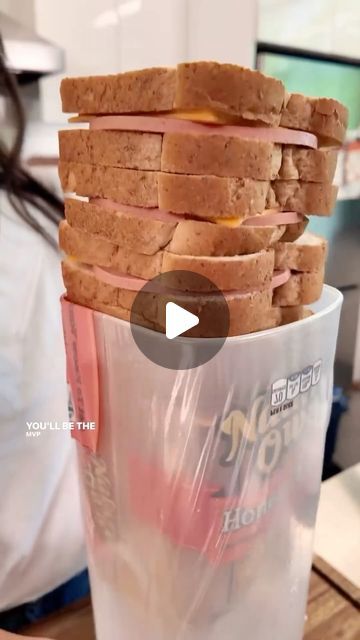 a stack of sandwiches sitting on top of a plastic cup next to a woman in a white shirt