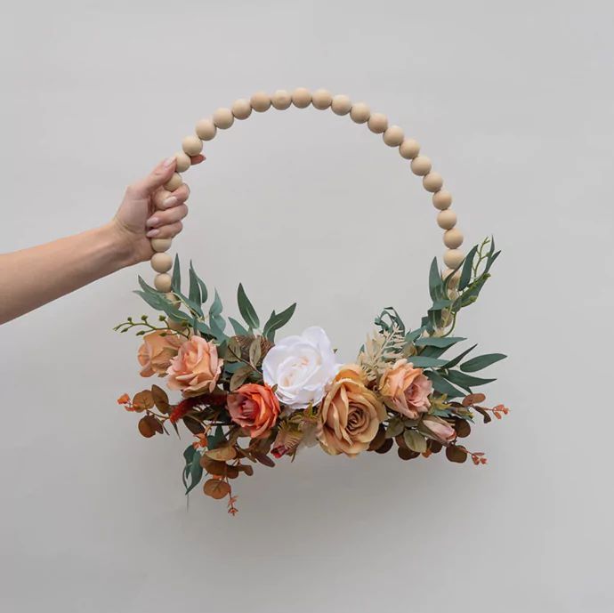 a hand holding a wooden beaded hoop with flowers and leaves on it's side