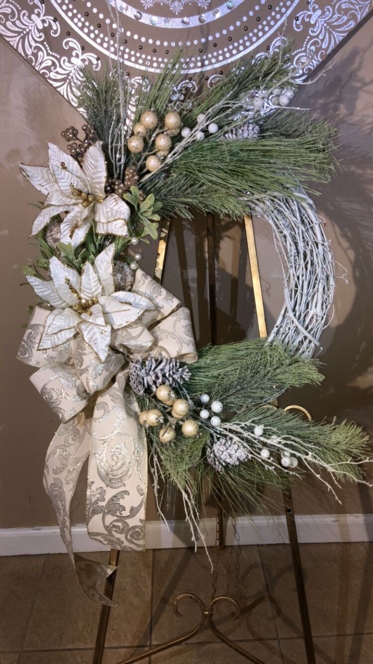 a wreath with white flowers and greenery on a stand in front of a wall