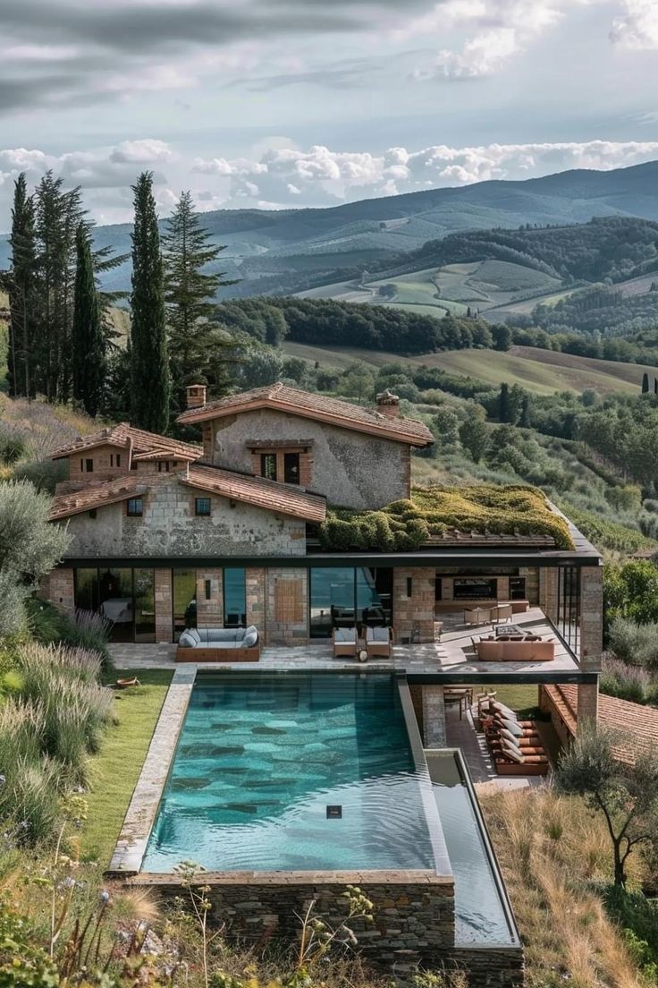 an outdoor swimming pool surrounded by greenery and hills in the distance is a house with a green roof