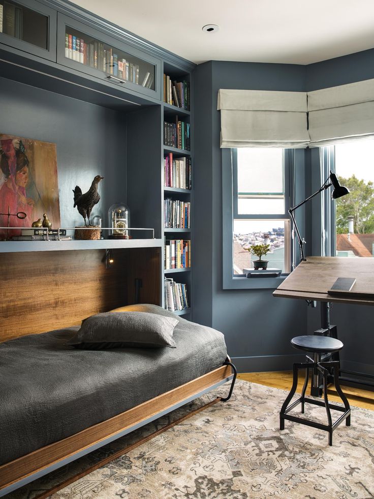 a bedroom with a bed, desk and bookshelf in the corner next to a window